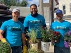 Three men hold plants in a garden during a community volunteer event